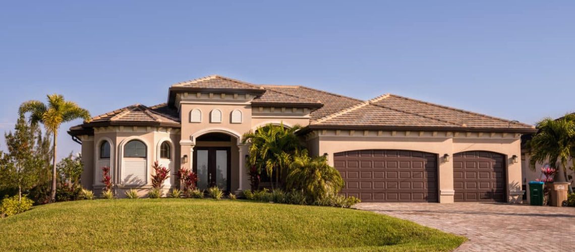 Typical Southwest Florida concrete block and stucco home in the countryside with palm trees, tropical plants and flowers, grass lawn and pine trees. Florida. South Florida single family house