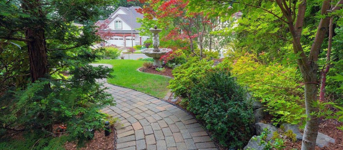 Garden brick paver path in frontyard with water fountain plants shrubs evergreen and deciduous trees landscaping