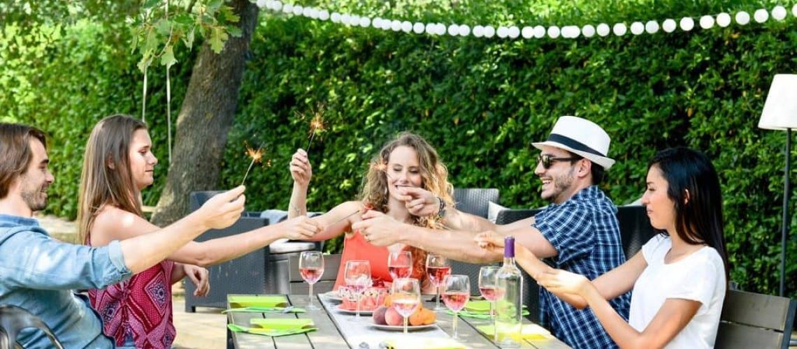 group of friends having fun picnic lunch party outdoor in backyard during summer holiday vacation